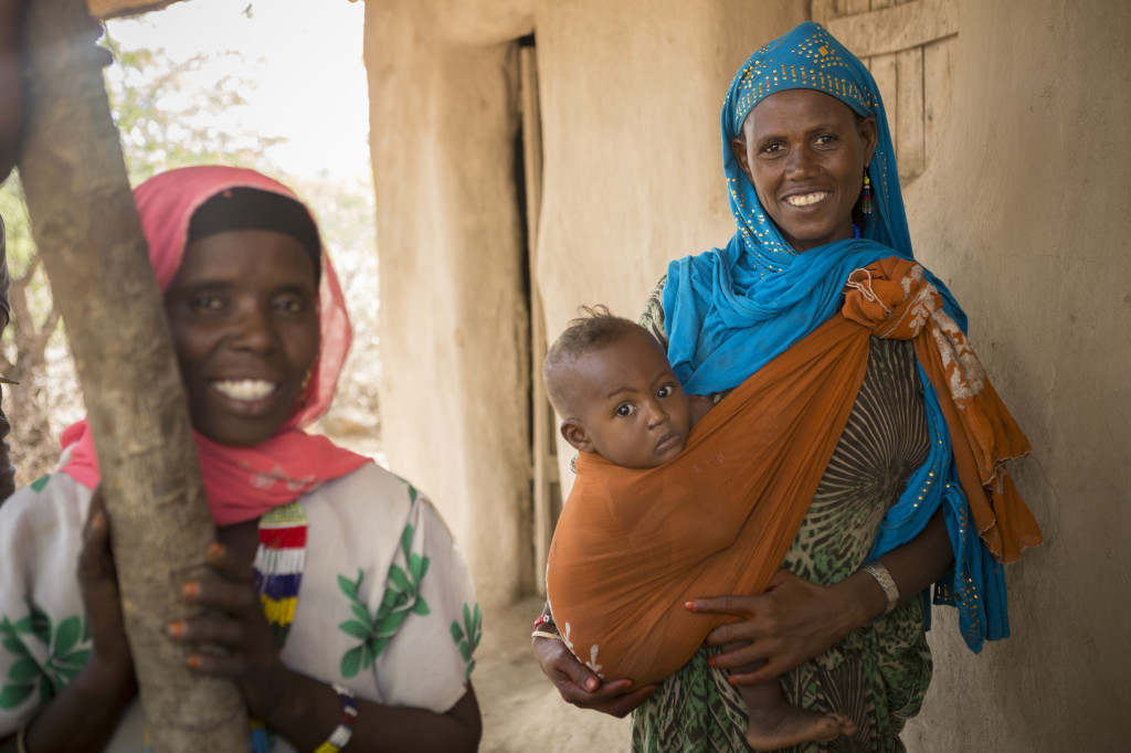 Caption: Hindi brings her eight-month-old son Jamal to an early childhood development center in the Fentale District of Ethiopia. Photo by Jake Lyell. tag = two women mother and son woman standing outdoors holding son on hip in orange wrap Original: Hindi Aliji (30) brings her young son Jamal (8 months) to an ECD centre in Fentale District, Ethiopia Ethiopia Food Crisis - Fentale District, Ethiopia December 4, 2015. Photo by Jake Lyell.